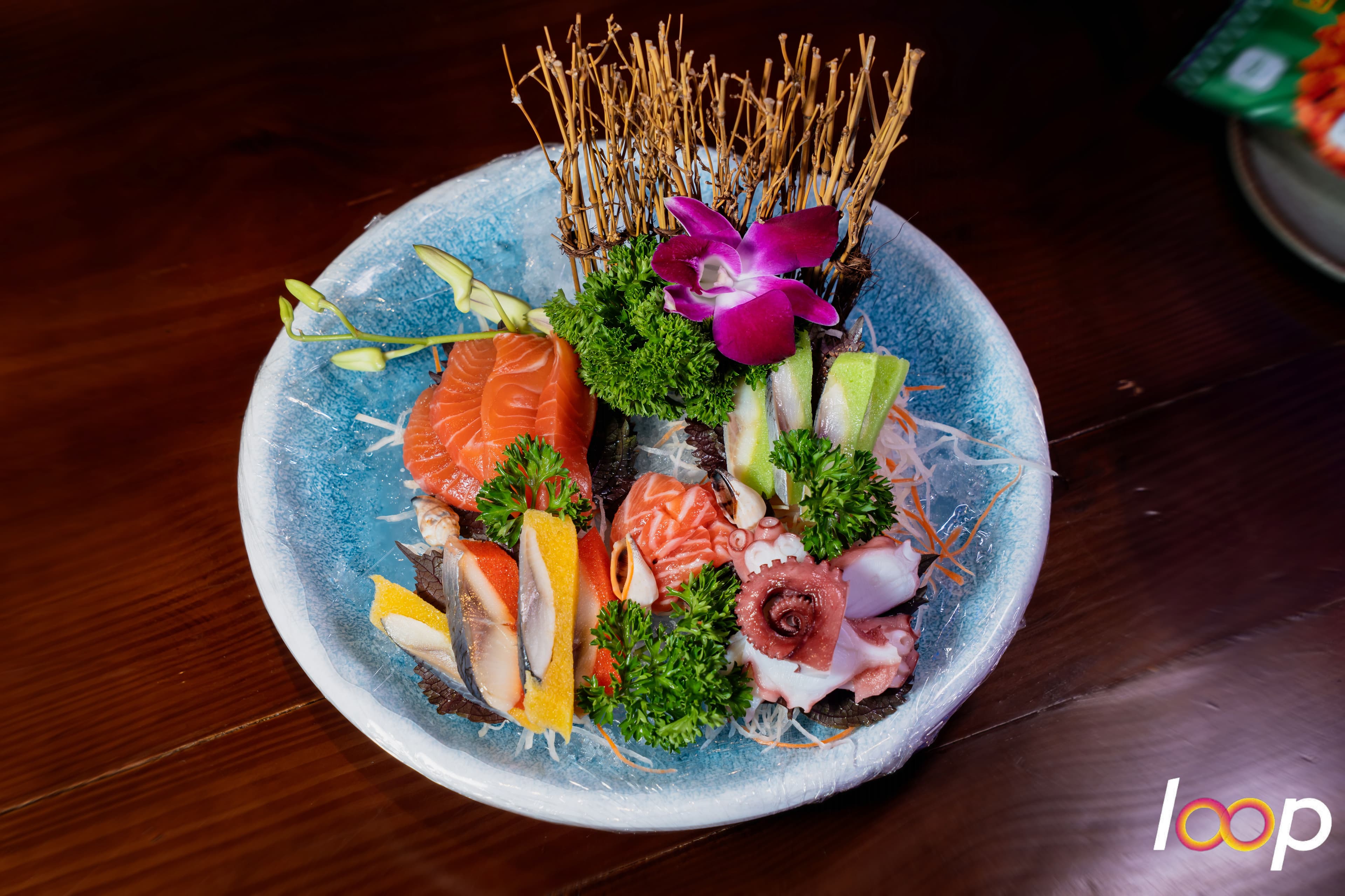 Đĩa sashimi cá hồi và bạch tuộc trang trí hoa lan trên bàn tiệc ở LOOP